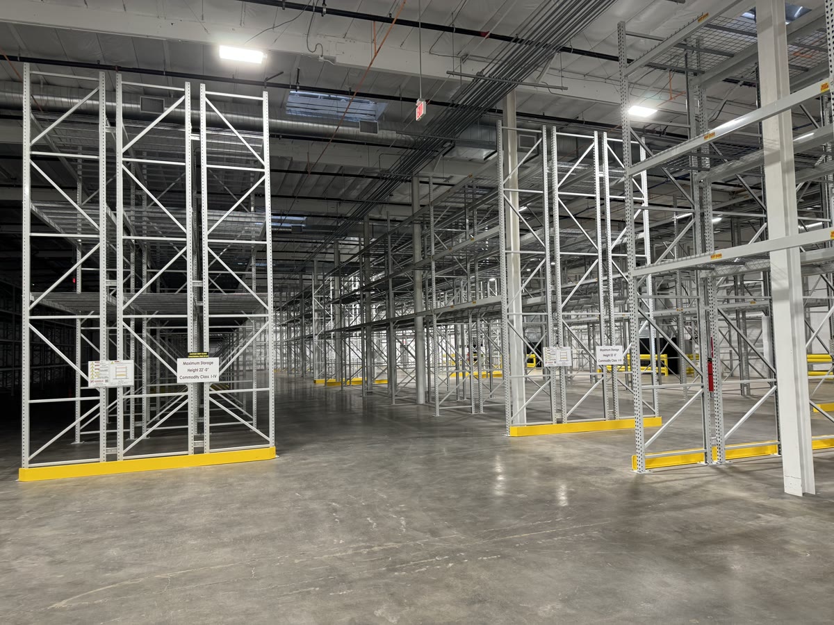 Tall selective pallet rack rows anchored to a thin concrete slab, with maximum storage height placards and base protectors